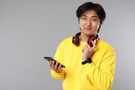 Handsome Asian man with headphones and smartphone on grey background. Space for textの写真素材