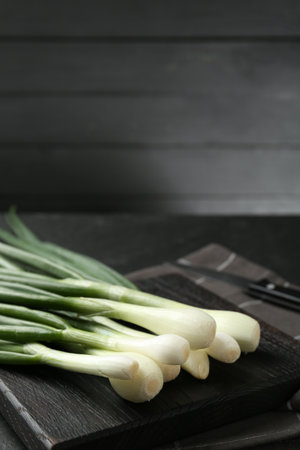 Fresh ripe green onions with cutting board and knife on black table, closeupの写真素材