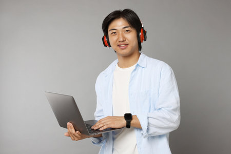 Handsome Asian man in headphones with laptop on grey backgroundの写真素材