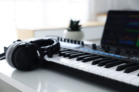 MIDI keyboard, headphones and laptop on white wooden table indoors, closeup