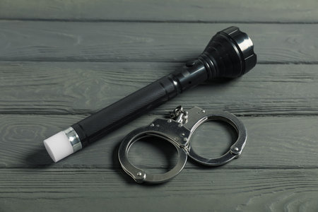 Flashlight and handcuffs on grey wooden table, closeup. Police equipmentの写真素材