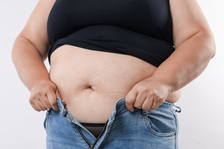 Overweight woman trying to put on tight jeans against white background, closeupの写真素材