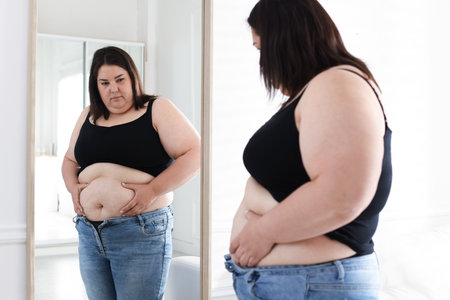 Woman with excessive belly fat near mirror indoors. Overweight problemの写真素材