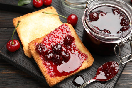 Toasts with tasty cherry jam and fresh fruits on black wooden table, closeupの写真素材