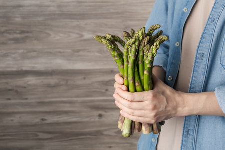 Woman holding fresh raw asparagus near wooden wall, closeup. Space for textの写真素材