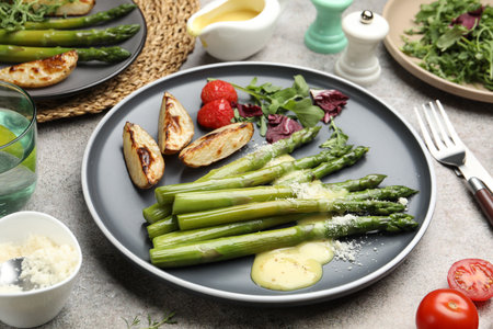 Tasty cooked asparagus served with baked potatoes, tomatoes and sauce on gray table, closeupの写真素材