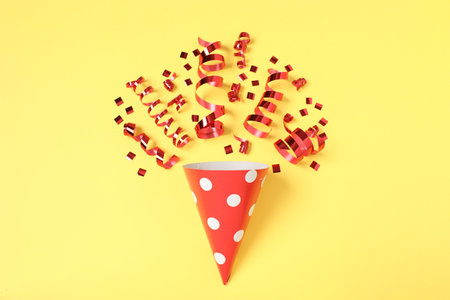 Shiny party streamers, confetti and cone on yellow background, flat layの写真素材