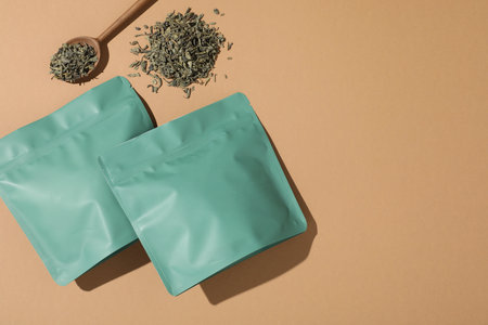 Zipper stand-up pouches and dry leaves on beige background, flat lay. Mockup for designの写真素材