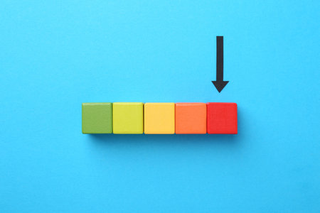 Maximum. Colorful cubes and arrow pointing at red one on light blue background, flat lay
