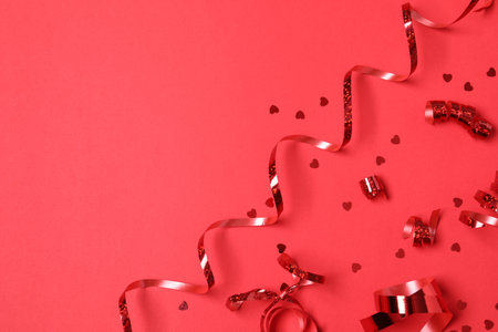 Shiny serpentine streamers and confetti on red background, flat lay. Space for textの写真素材