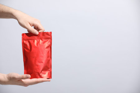 Woman holding blank zipper stand-up pouch on light gray background, closeup. Space for text
