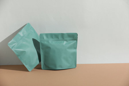 Zipper stand-up pouches on beige table against light gray background, mockup for design