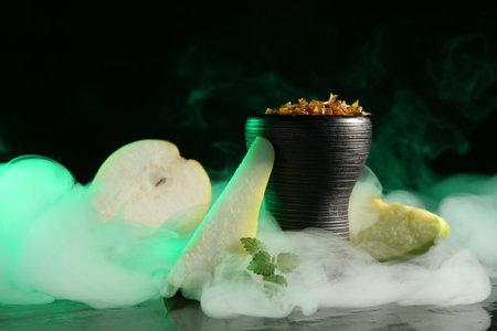 Hookah bowl with pear pieces, mint and smoke on black table, closeup