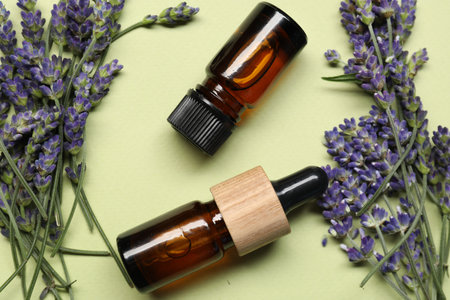 Natural essential oil and lavender flowers on light green background, flat layの写真素材