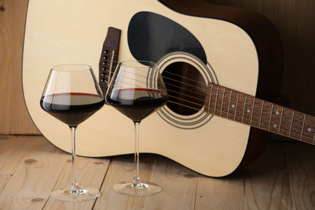 Acoustic guitar and glasses of red wine on wooden tableの写真素材