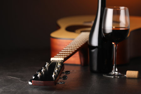 Acoustic guitar and red wine on black table with brown light, closeupの写真素材