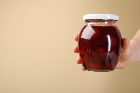 Woman with tasty cherry jam on beige background, closeup. Space for textの写真素材