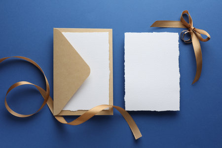 Wedding invitation cards, envelope, golden rings and ribbon on blue background, flat layの写真素材