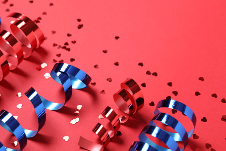 Shiny serpentine streamers and confetti on red background, above view. Space for textの写真素材