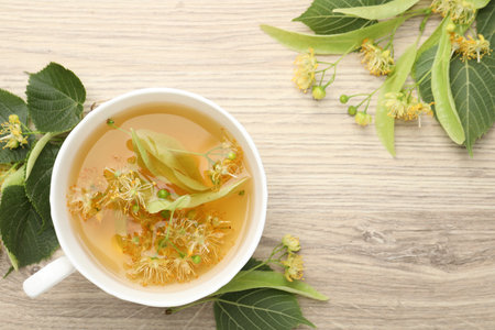Fresh linden tea in cup and flowers on wooden table, flat lay. Space for textの写真素材