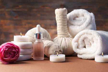 Massage bags, stones, towels, cosmetic product, peony flower and burning candles on dark beige table. Spa compositionの写真素材