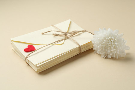 Stack of love letters, flower and red heart on beige background