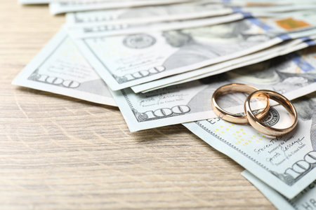 Gold wedding rings and dollar banknotes on wooden table, closeup. Space for textの写真素材