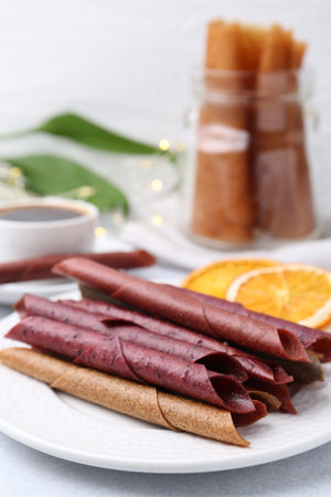 Tasty fruit leather rolls and orange slices on white table, closeup