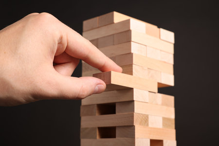 Lviv, Ukraine - December 08, 2023: Playing Jenga. Man removing wooden block from tower on dark background, closeupの写真素材