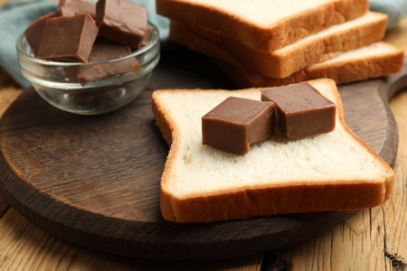Tasty chocolate butter cubes on slice of bread on wooden table, closeupの写真素材