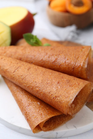 Delicious fruit leather rolls, mint, mango and apricots on table, closeup