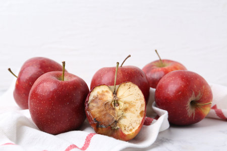 Spoiled apple and good ones on white table, closeup