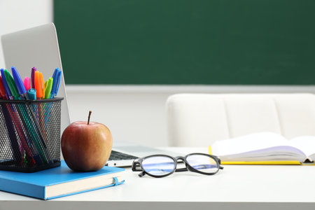 Different school stationery, laptop, glasses and apple on white table near blackboard indoors, closeupの写真素材