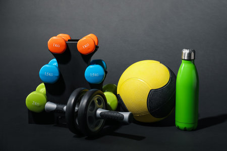 Medicine ball, dumbbells, ab wheel and water bottle on black backgroundの写真素材