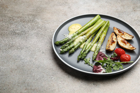 Tasty cooked asparagus served with baked potatoes, tomatoes and sauce on gray table, closeup. Space for textの写真素材