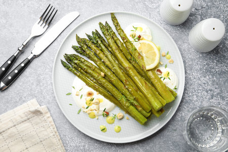 Tasty cooked asparagus served with lemon and sauce on gray table, flat layの写真素材