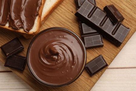 Tasty chocolate butter, pieces and sandwiches on wooden table, top view