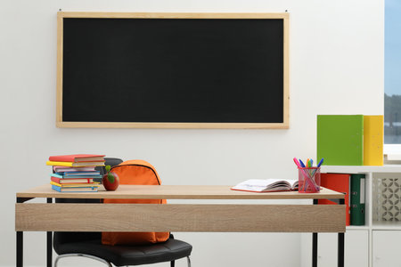 Different stationery and red apple on wooden table near blackboard indoorsの写真素材