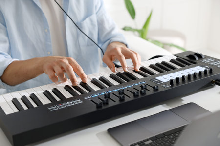 Man working with MIDI keyboard at white table indoors, closeup