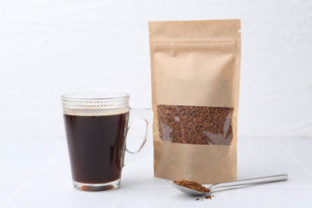 Instant coffee in bag, spoon and cup of drink on light tableの写真素材