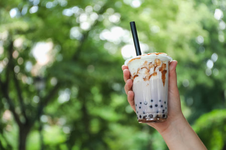 Woman with tasty milk bubble tea in plastic cup outdoors, closeup. Space for textの写真素材