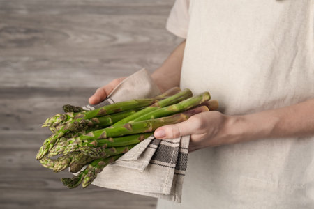 Woman holding fresh raw asparagus near wooden wall, closeupの写真素材