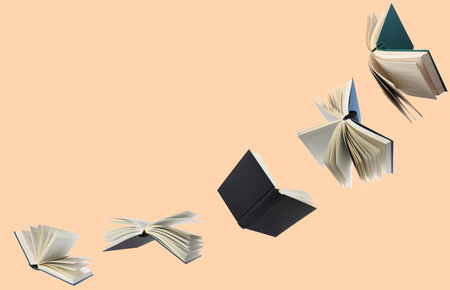 Hardcover books flying like birds against pink beige backgroundの写真素材