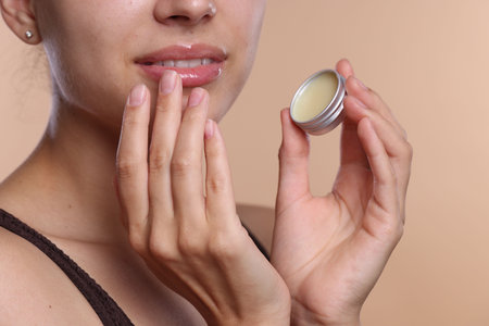 Young woman with lip balm on beige background, closeupの写真素材