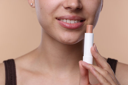 Young woman with lip balm on beige background, closeupの写真素材