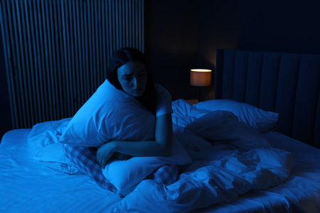 Frustrated woman with pillow suffering from insomnia on bed at homeの写真素材