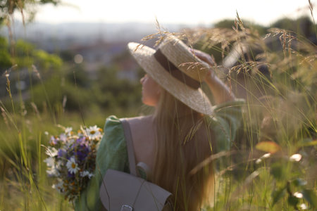 Woman with beautiful wildflowers, hat and backpack in meadow on sunny day, back viewの写真素材
