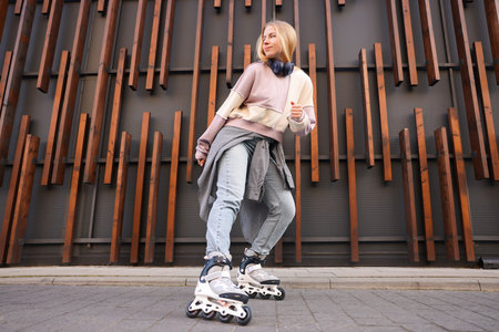 Beautiful young woman with roller skates near building outdoors, low angle view