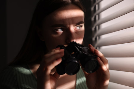Paranoia. Worried woman with binoculars near window indoorsの写真素材