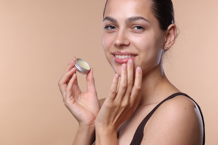 Young woman with lip balm on beige backgroundの写真素材